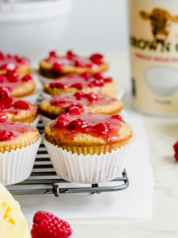 Glazed lemon poppyssed muffins on a wire rack with a container of yogurt in the background.