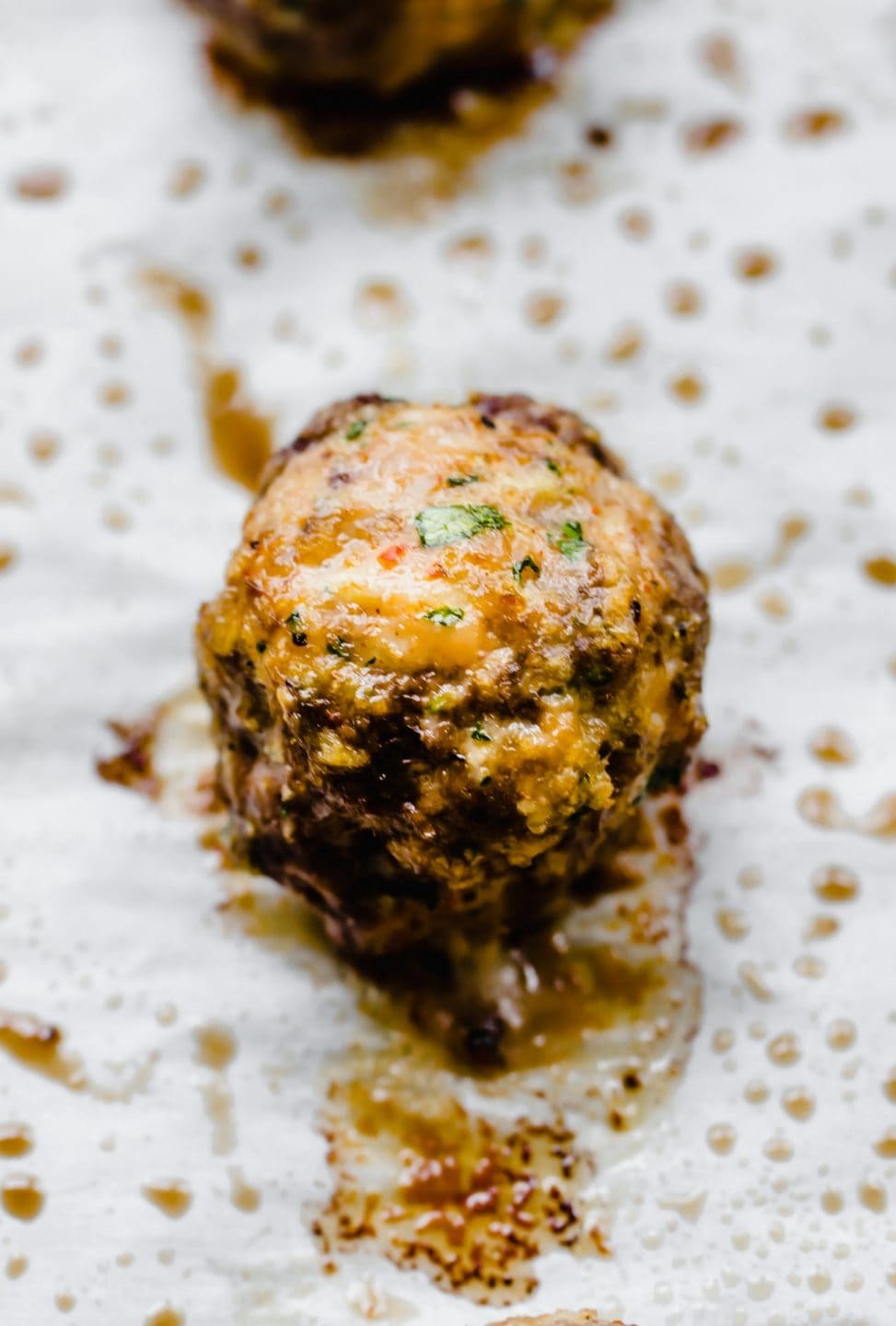 A baked Italian meatball on a parchment paper-lined baking sheet.