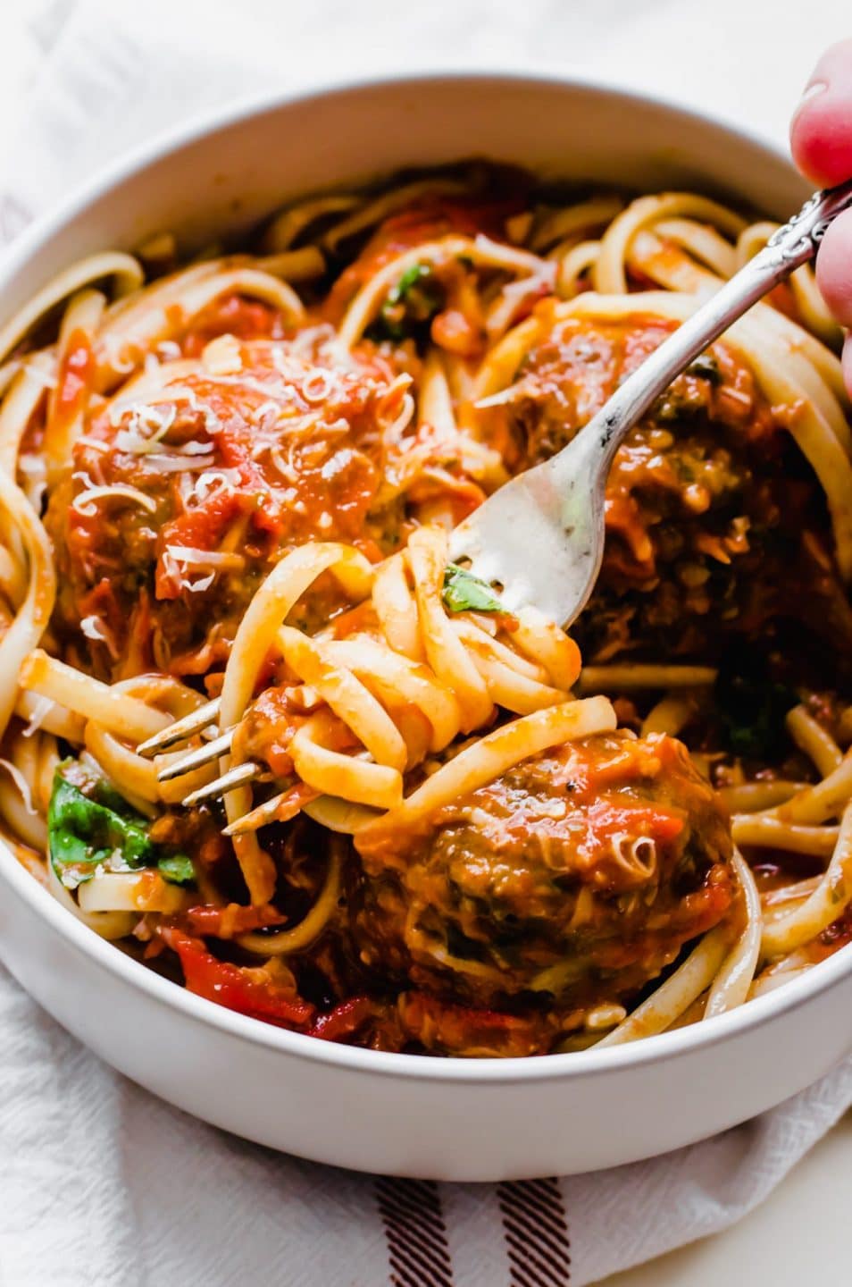 A fork twisting noodles from a bowl of spaghetti and meatballs. 