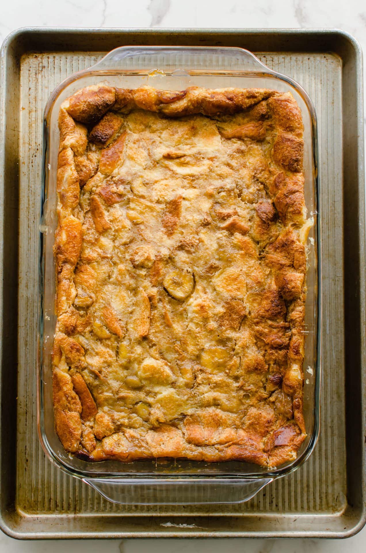 Baked bread pudding in a glass dish on a sheet pan.