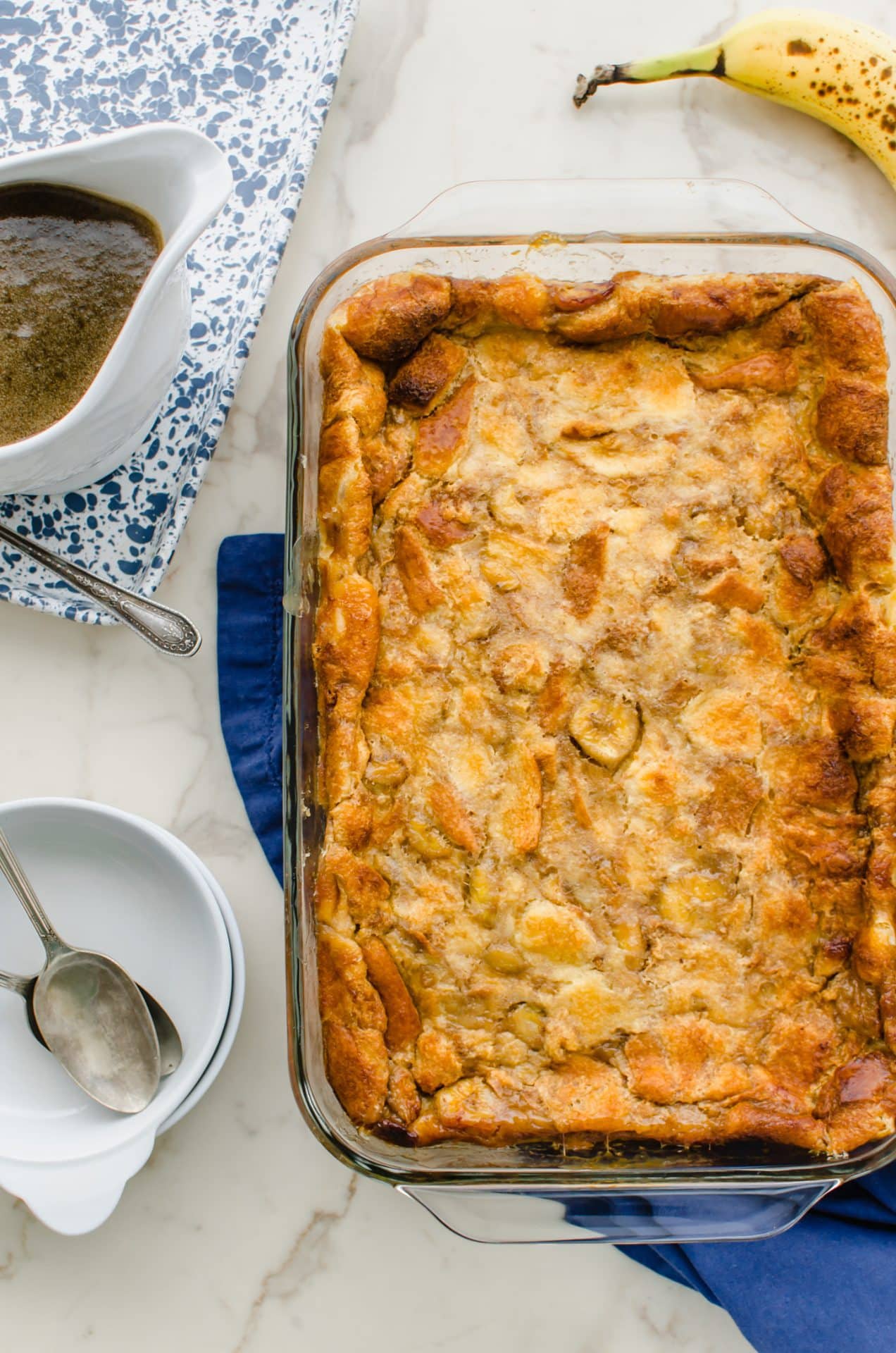 Baked bread pudding on a blue napkin with a gravy boat of sauce on the side.