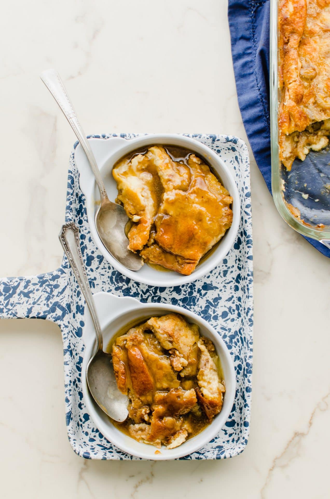 Bread pudding in white dishes on a speckled blue tray.