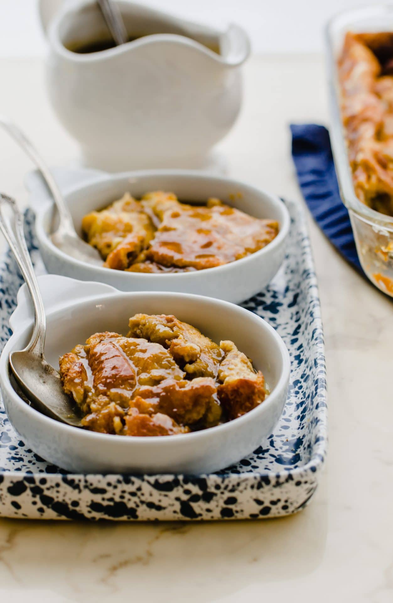 Bread pudding with sauce on top in a white dish with a spoon on the side.