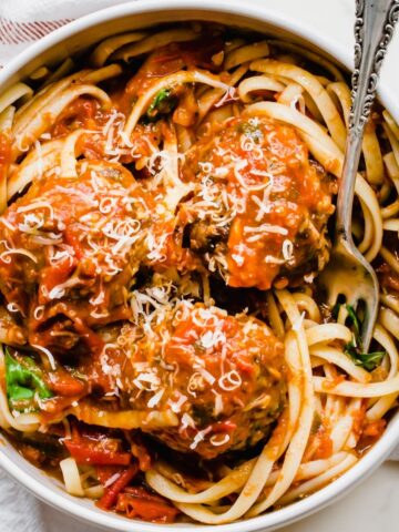A bowl of spaghetti and meatballs with a fork on the side.