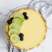 A fresh lime tart with sliced lime and blackberries on top. This is an overhead view and on a white marble background.
