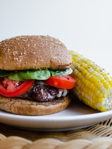Hamburger on a plate with an ear of corn as a side.