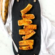 Overhead view of a slate tray with roasted plantains distributed over the top. Cinnamon is sprinkled on top of the plantains.