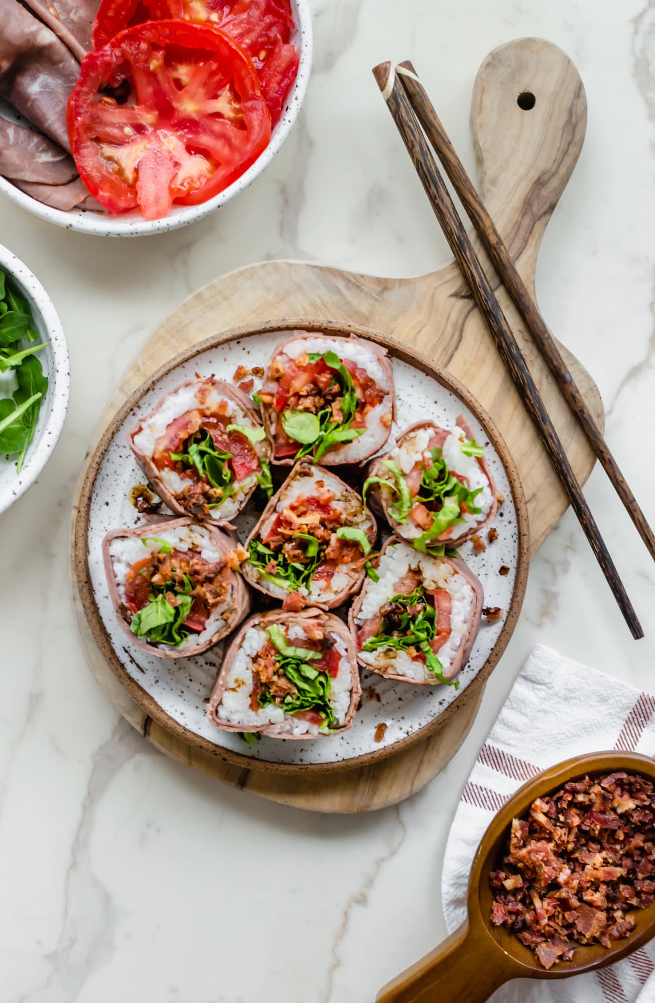 A plate of Beefshi BLT roll on a cutting board with chopsticks on the side.