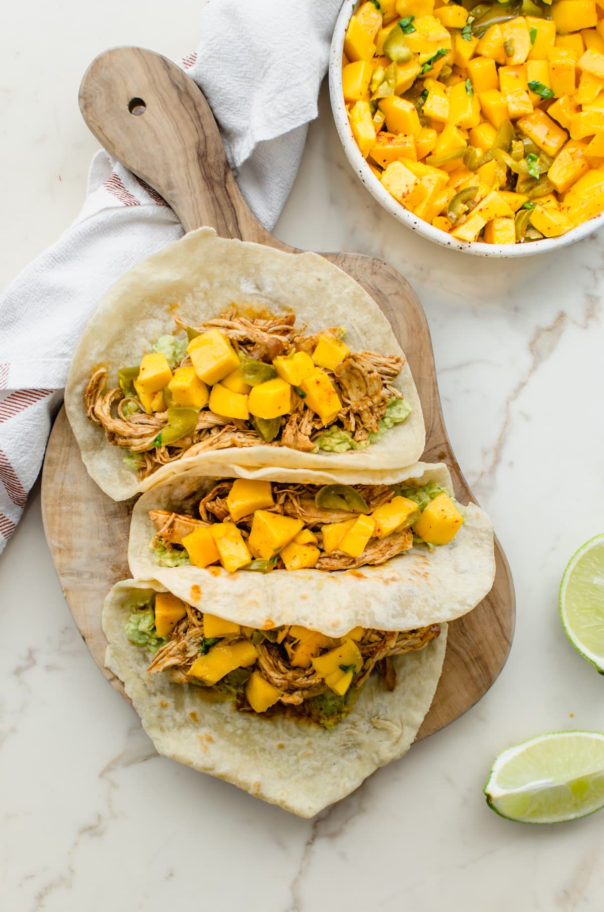 Three chicken tacos with mango salsa on a wood cutting board. 