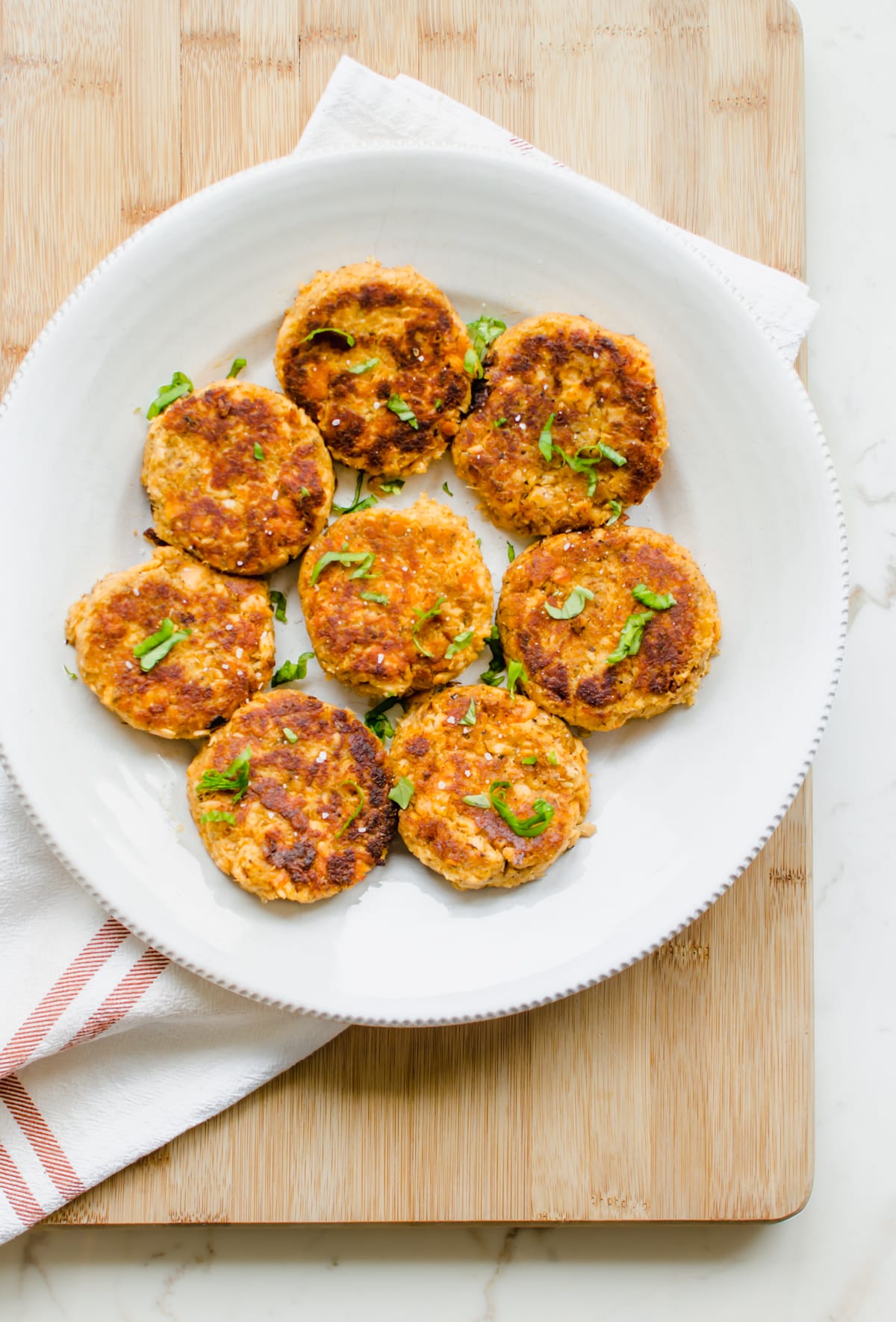 Cooked salmon cakes on a white plate garnished with strips of fresh basil. 