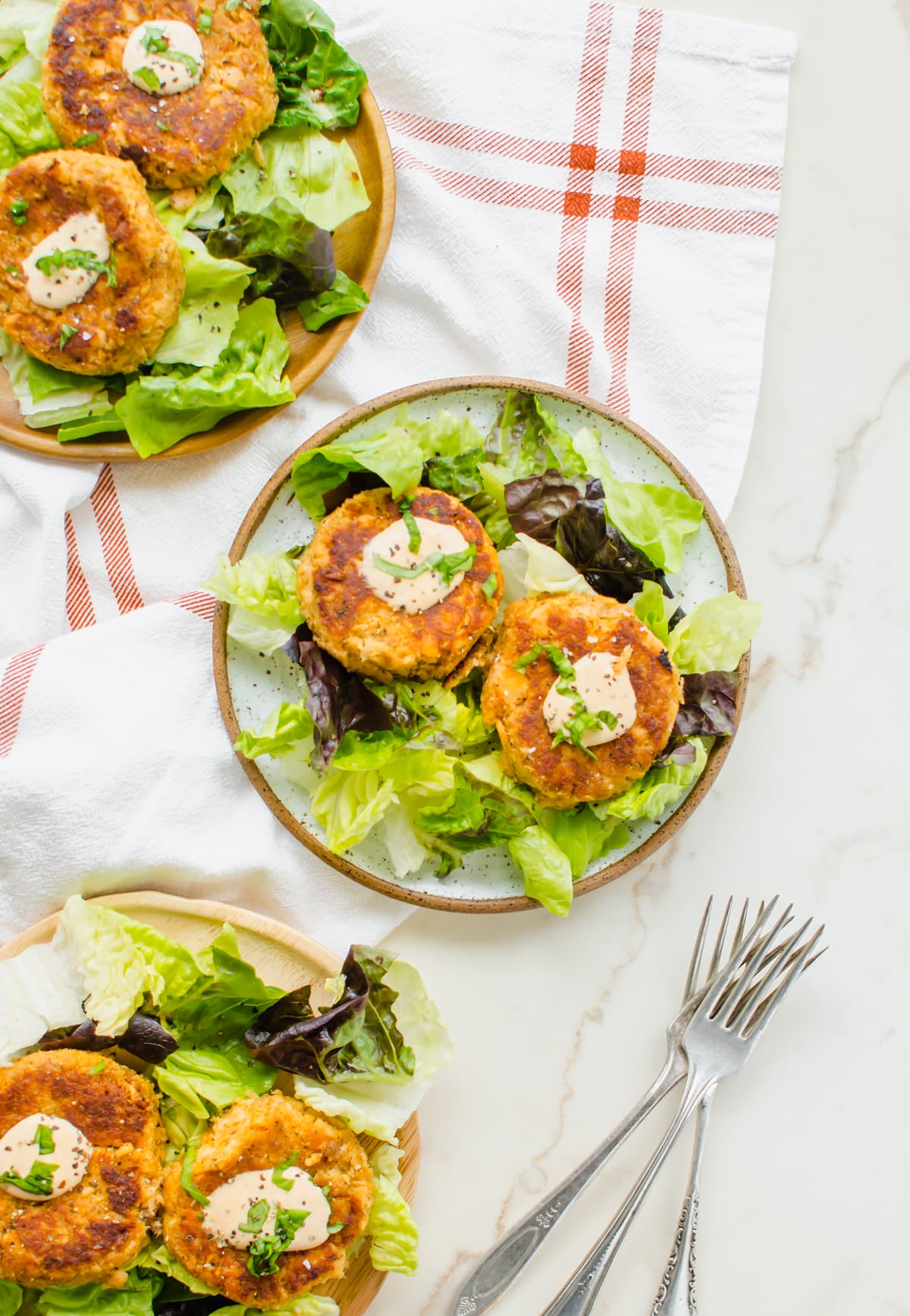 Three plates with a salad and salmon cakes topped with hot sauce aioli. 