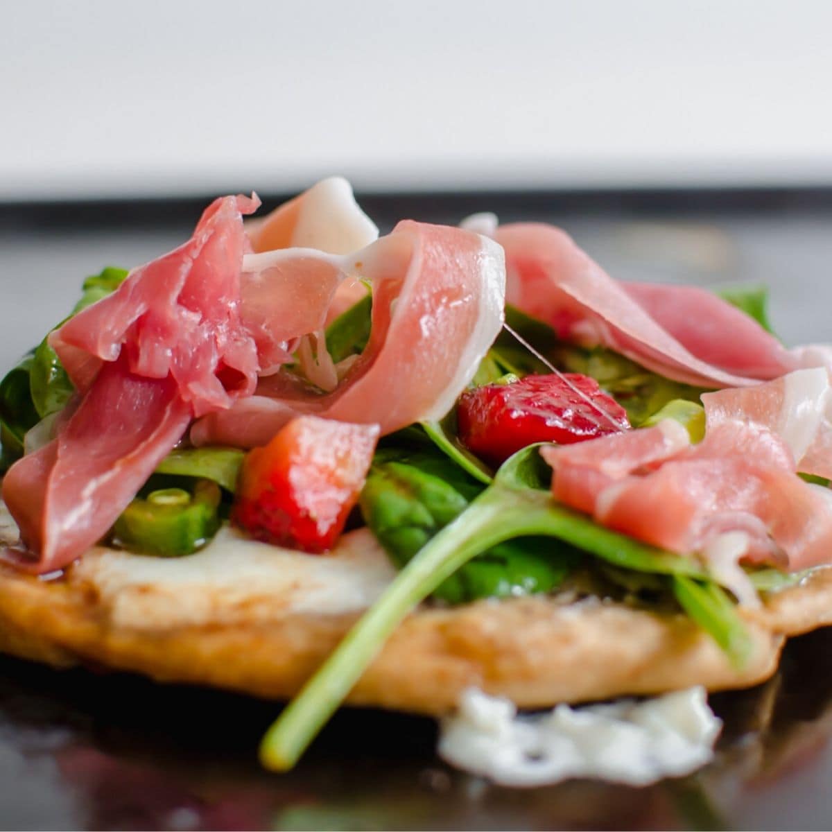 Side view of a mini salad pizza with greens, prosciutto, and asparagus on mozzarella.