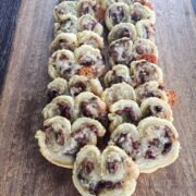 Olive cheddar palmiers cut into coins and lined up on a wooden serving tray.