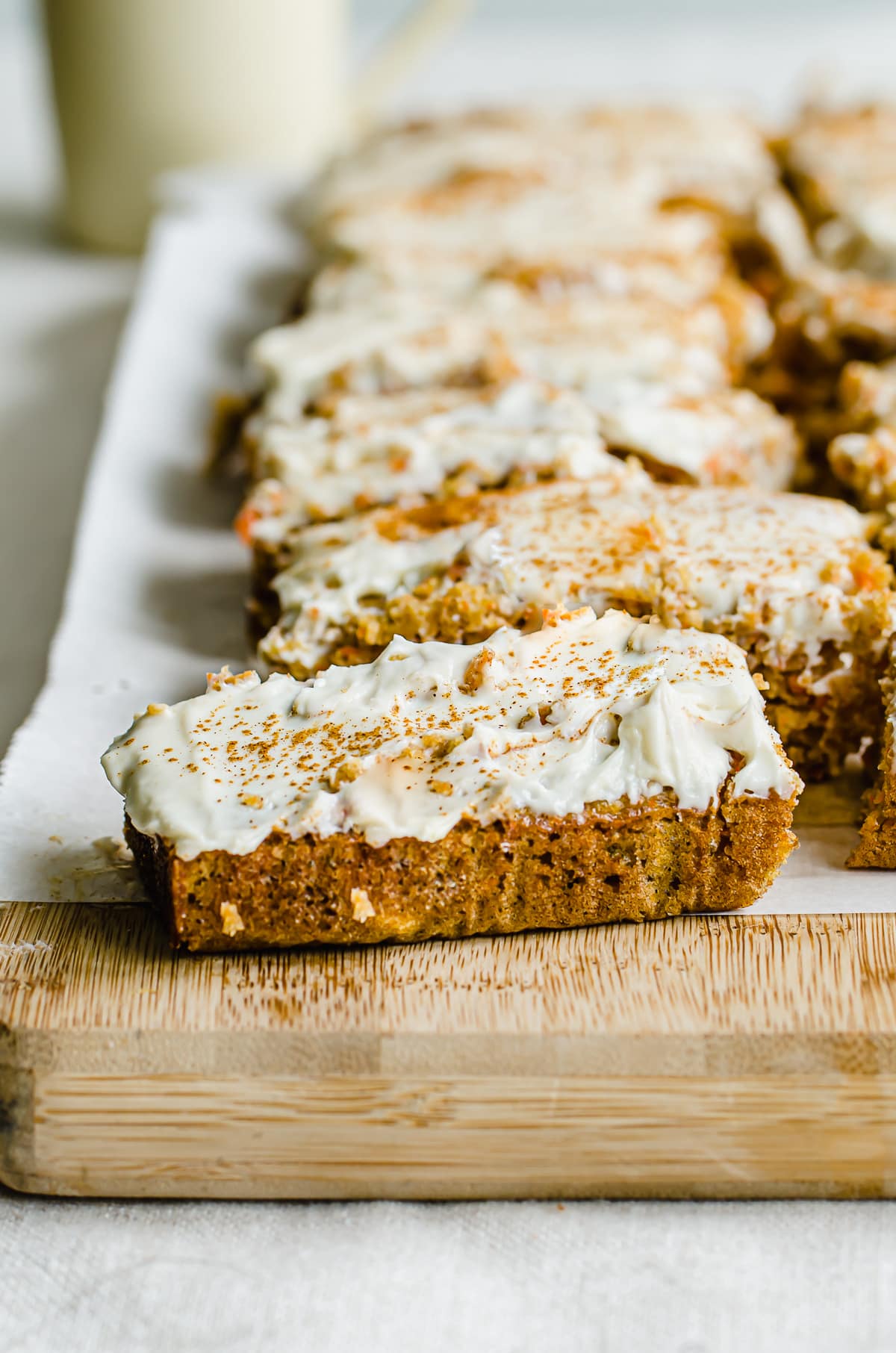 A slice of carrot cake pulled out from other slices on a cutting board.