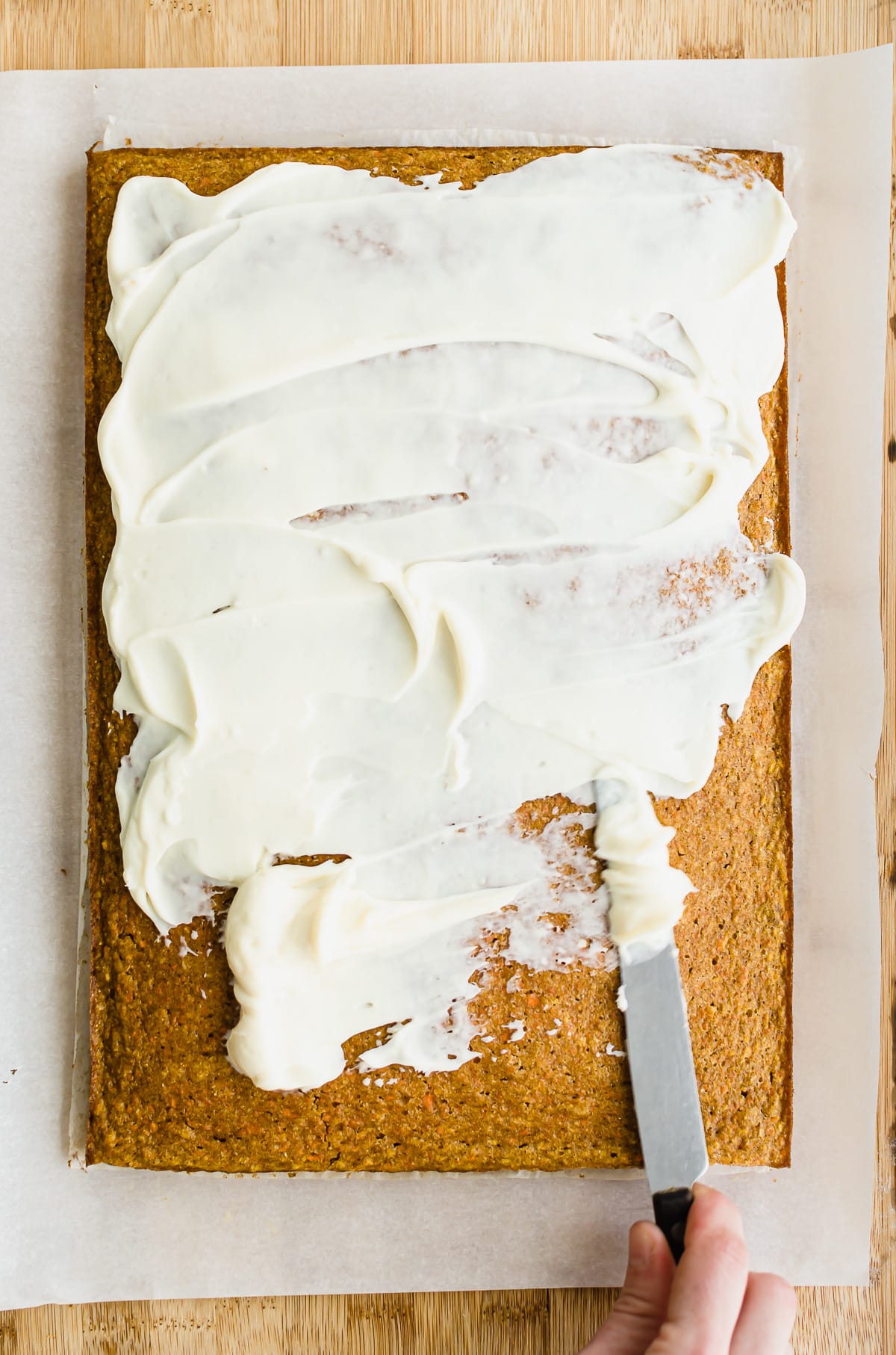 A knife spreading honey cream cheese frosting on a cake.