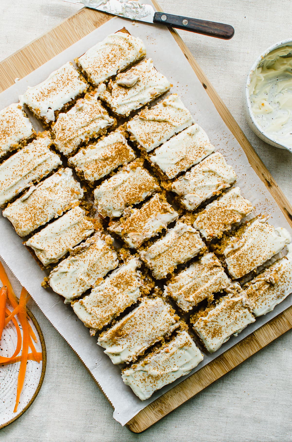 Carrot cake sliced into bars on a parchment paper lined cutting board.