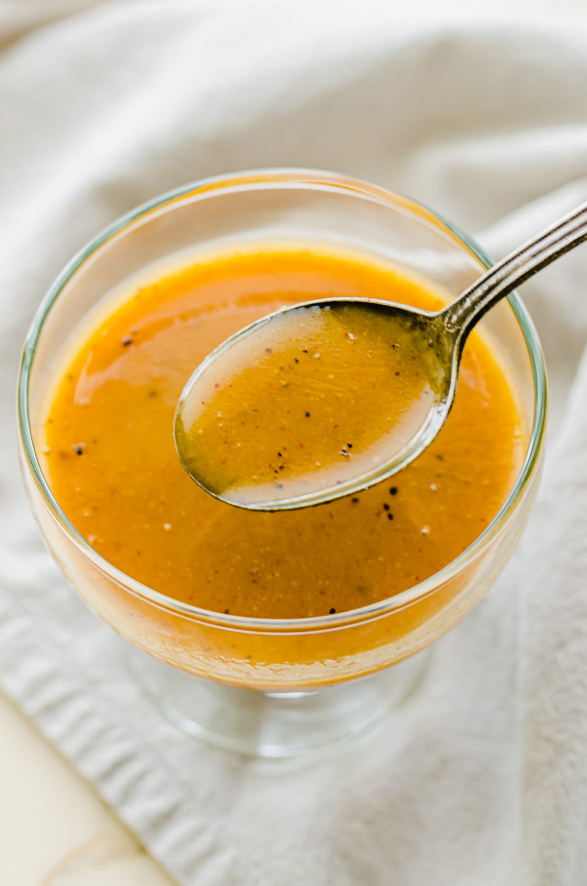 A glass bowl filled with honey mustard dressing with spoon scooping some out of the bowl.