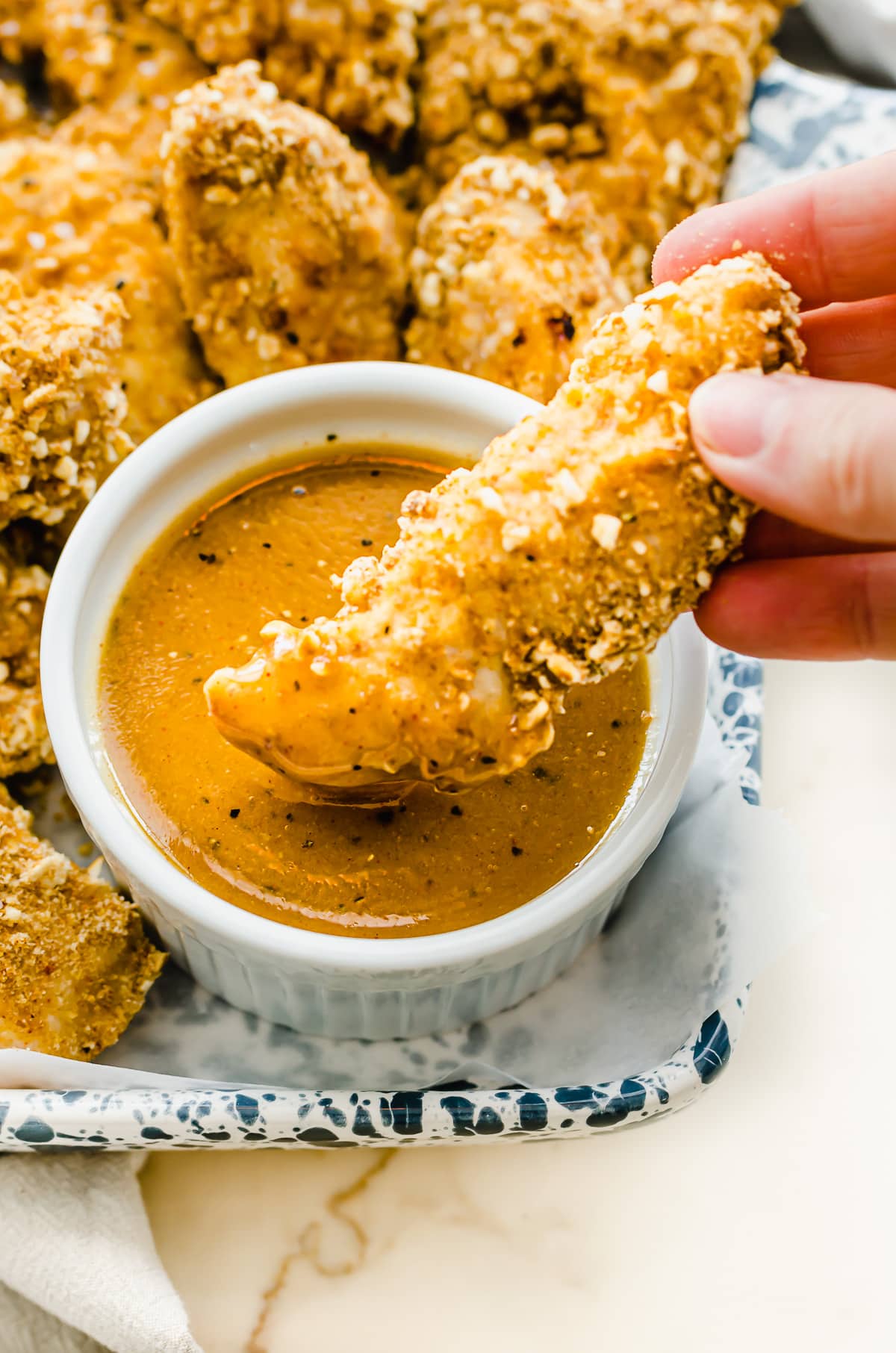 A chicken finger being dipped into a bowl of honey mustard dressing.