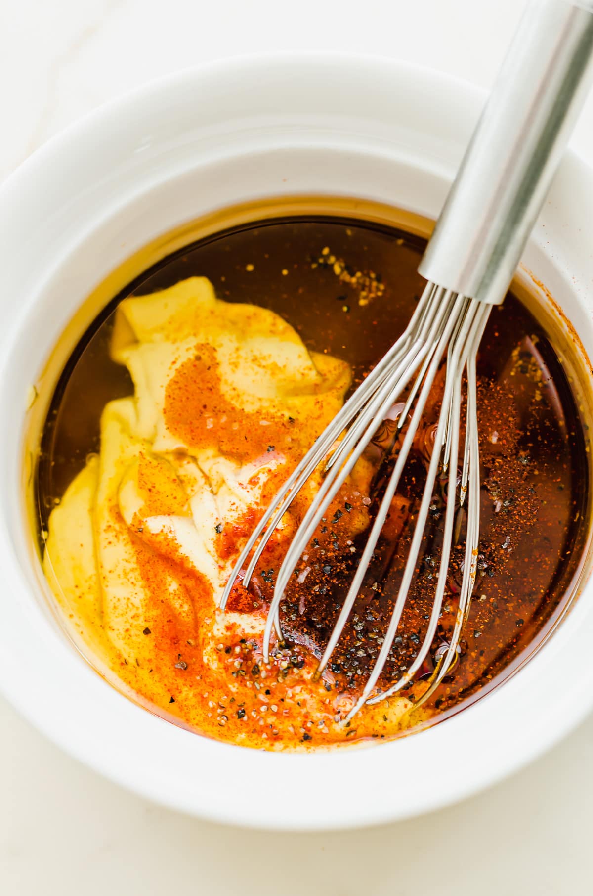 A whisk combining ingredients for honey mustard dressing in a white bowl. 