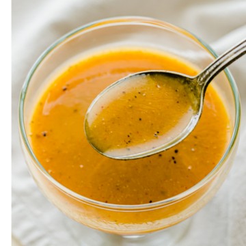 A spoon dipping into a glass bowl of honey mustard dressing.