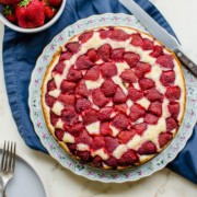A strawberry buttermilk cake on a floral plate with a knife and bowl of strawberries on the side.