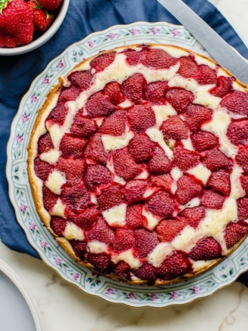 A strawberry buttermilk cake on a floral plate with a knife and bowl of strawberries on the side.