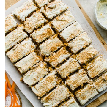 Carrot cake sliced into bars on a parchment paper lined cutting board.