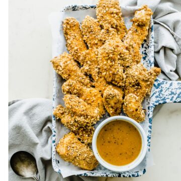 A blue and white tray filled with pretzel chicken strips and a bowl of honey mustard dip.