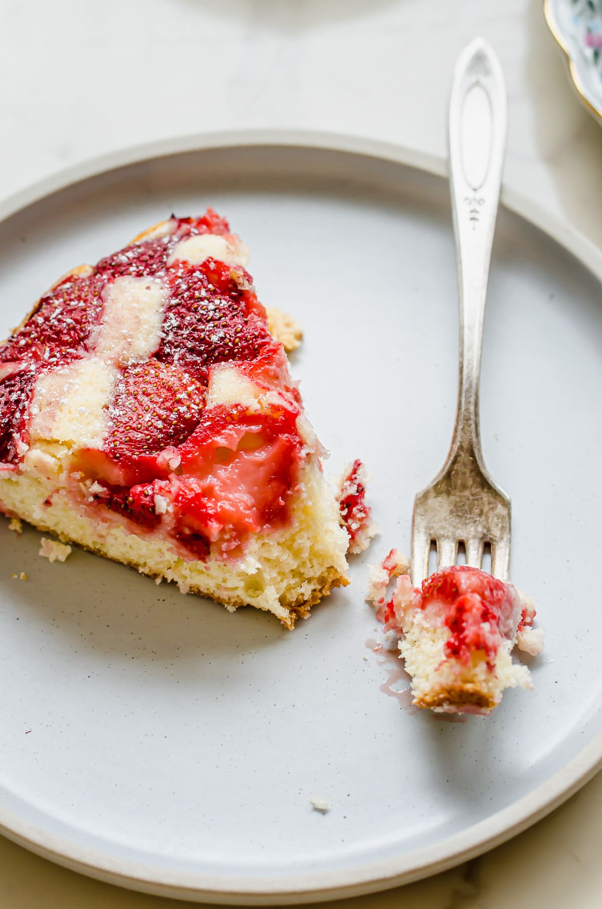 A fork with a bite of strawberry cake on a plate with the sliced cake.