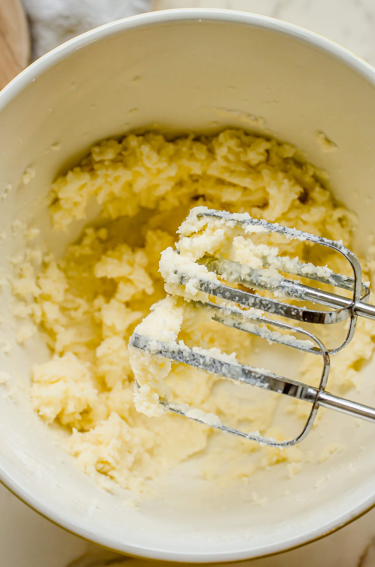 Creamed butter and sugar in white bowl with beaters.