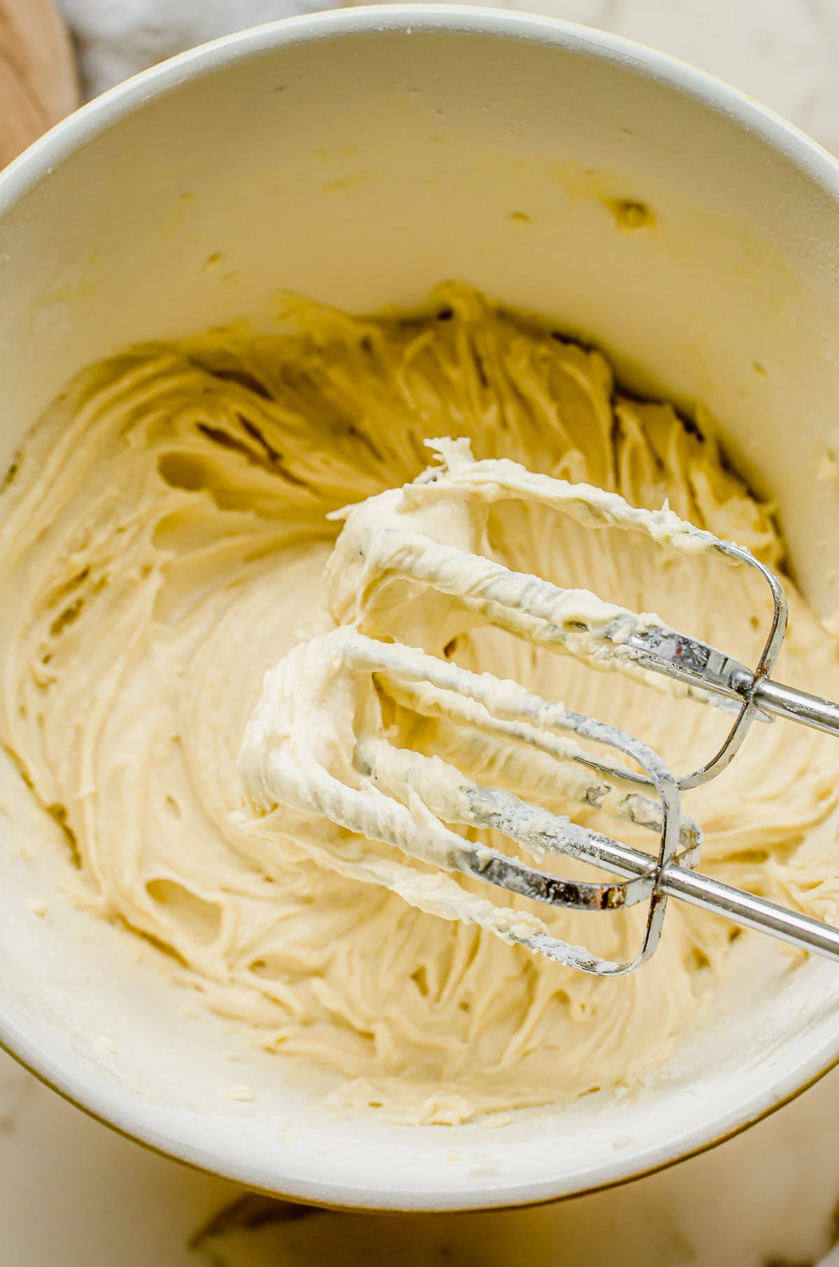 Creamed butter cake batter in a white bowl with beaters in the batter.