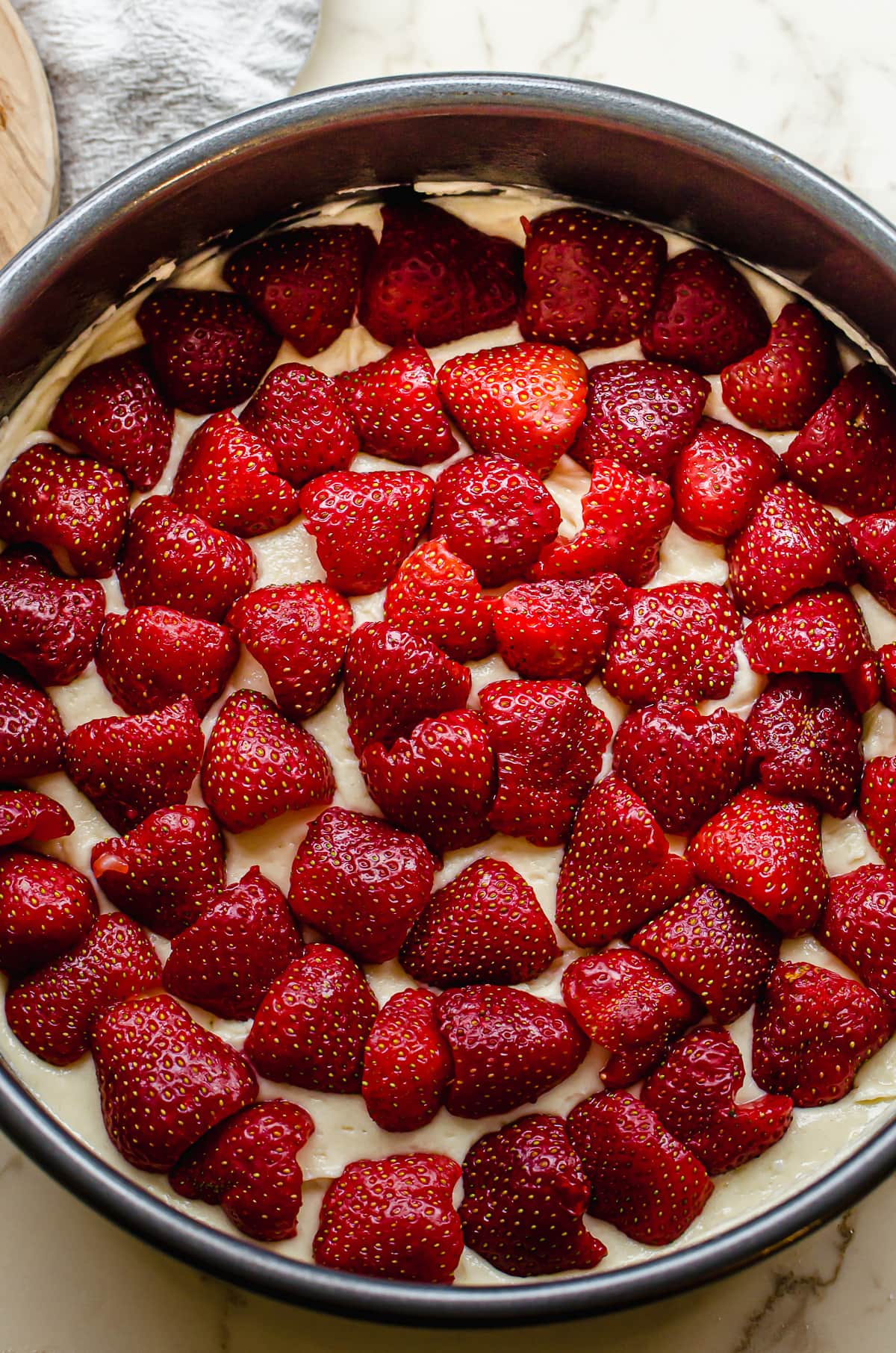 An unbaked pan of cake batter topped with fresh strawberries in a circular patterns.