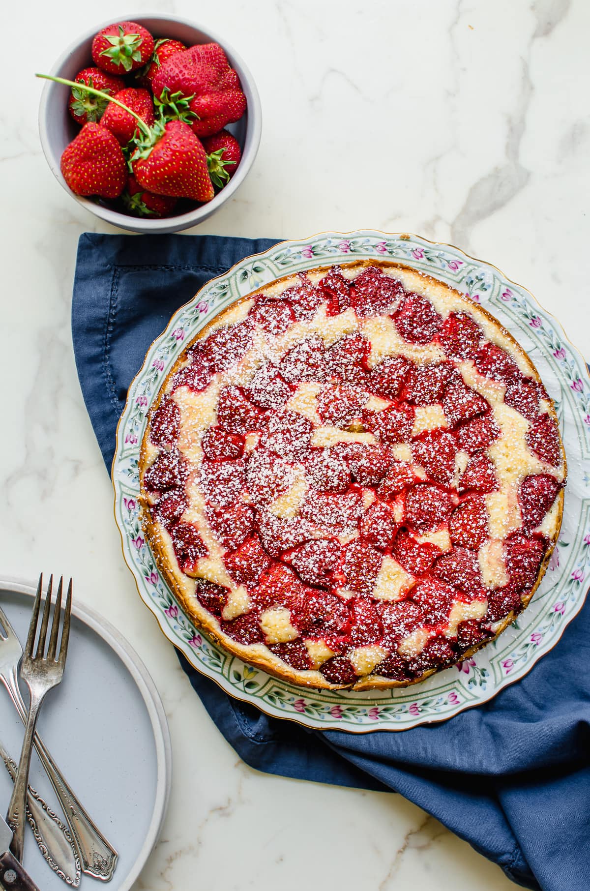 A bake strawberry buttermilk cake sprinkled with powdered sugar on a floral plate.