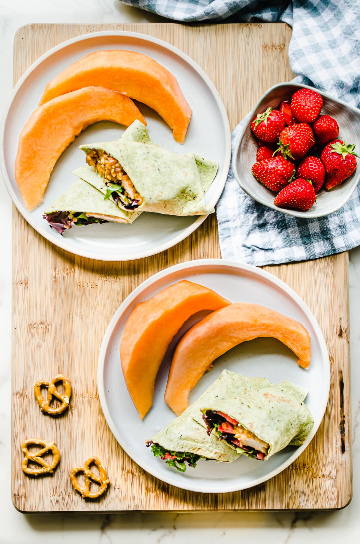 Overhead shot of two blue plates with sliced chicken wraps and slices of cantaloupe with a side of strawberries.