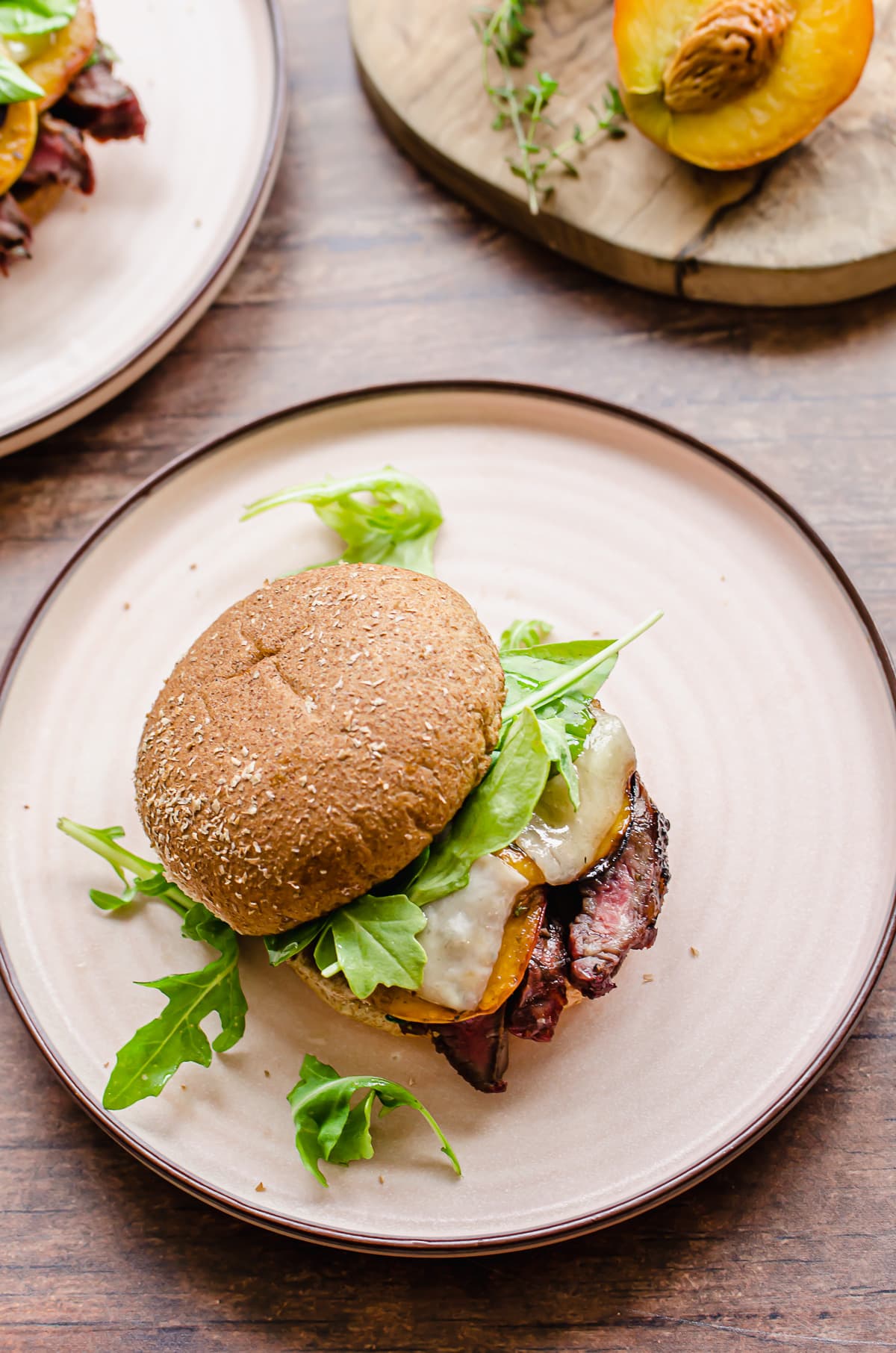 Overhead shot of a steak sandwich with arugula and peaches on a pink plate.