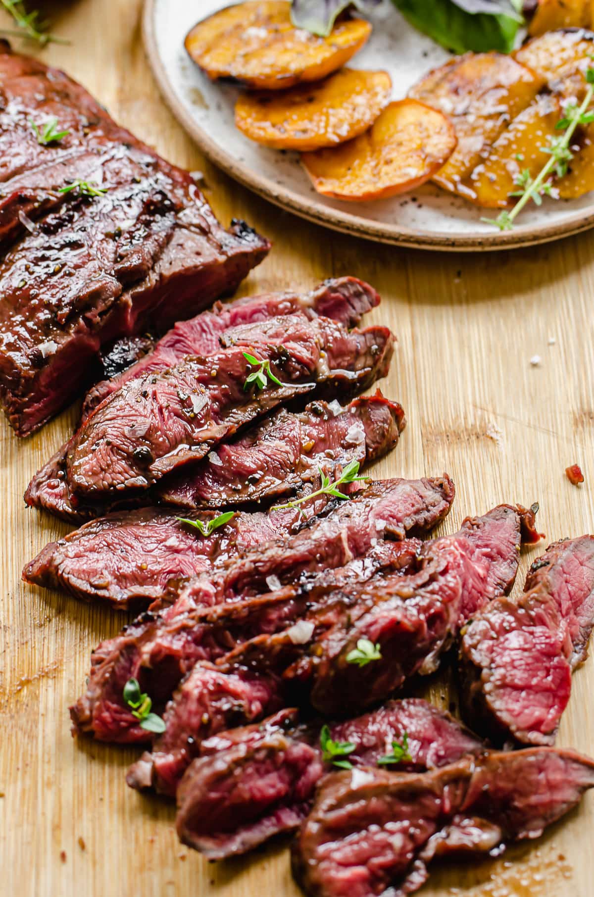 Thinly sliced steak on a cutting board with a plate of grilled peaches on the side.