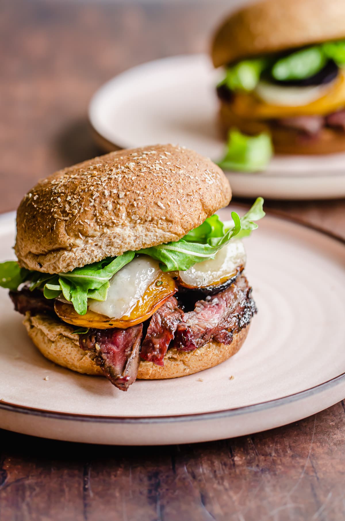 Straight-on shot of a steak sandwich on a wheat bun with lettuce, cheese, and peaches.