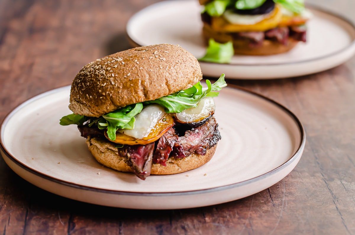 Side shot of a steak sandwich with arugula and peaches on a pink plate.