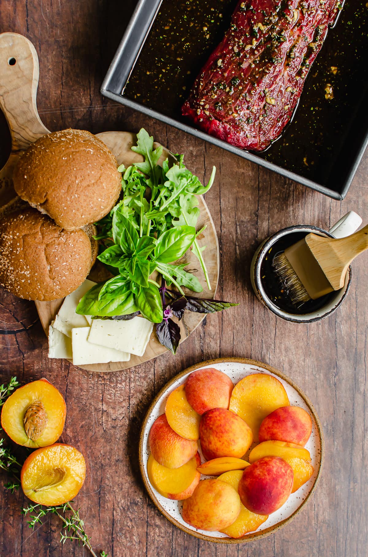 Measured ingredients for grilled steak sandwiches with peaches on a wood background.