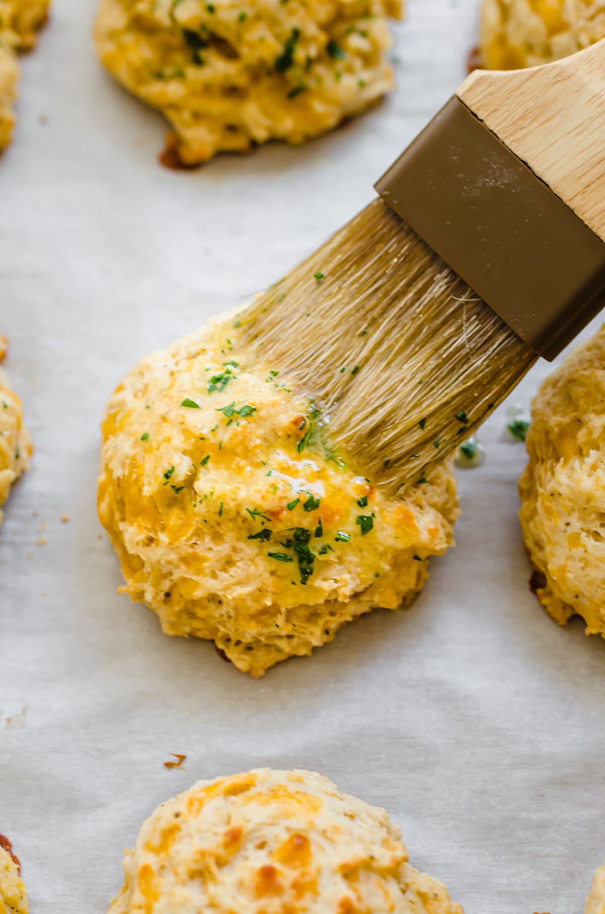 A brush spreading on butter herb topping on a cheddar bay biscuit.