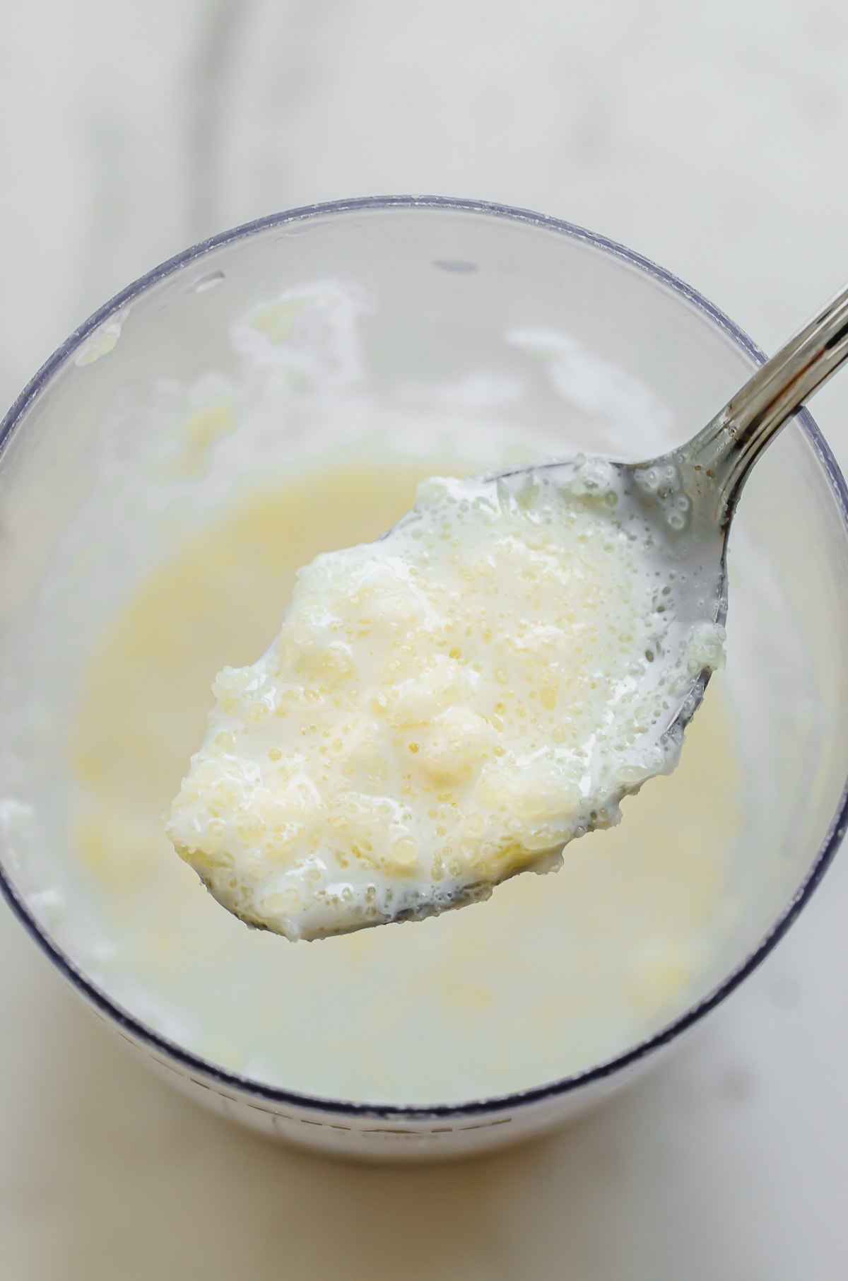 A spoonful of butter clumped in buttermilk being lifted out of a measuring cup.