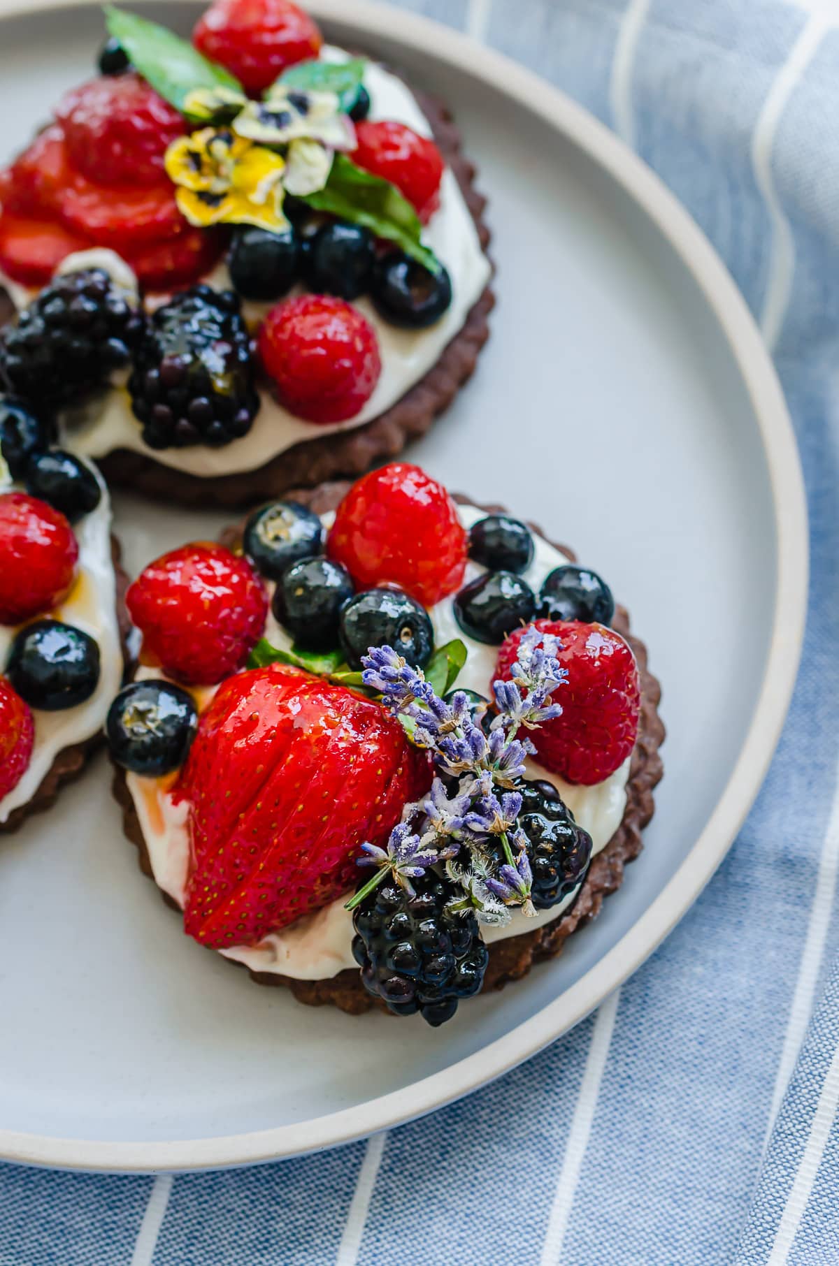 Side shot of a chocolate mini fruit tart on a blue plate.