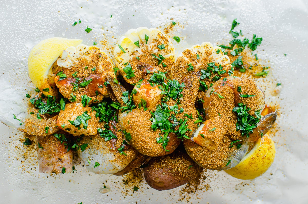 Seasoned shrimp, corn, and potatoes with parsley on a piece of foil.