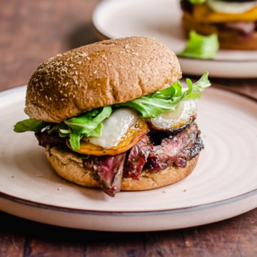 A grilled steak sandwich with peaches on a pink rimmed plate.