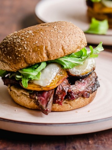 A grilled steak sandwich with peaches on a pink rimmed plate.