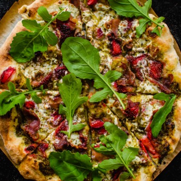 A prosciutto pizza with strawberries and arugula.