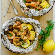Two bowls with foil packs of grilled shrimp, corn, and potatoes.