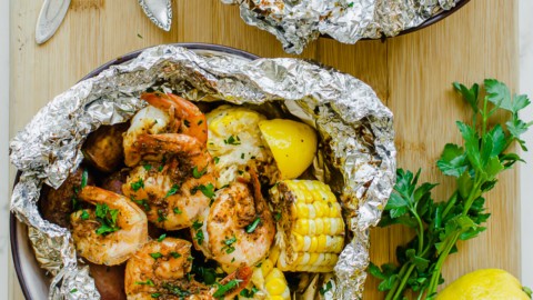Two bowls with foil packs of grilled shrimp, corn, and potatoes.