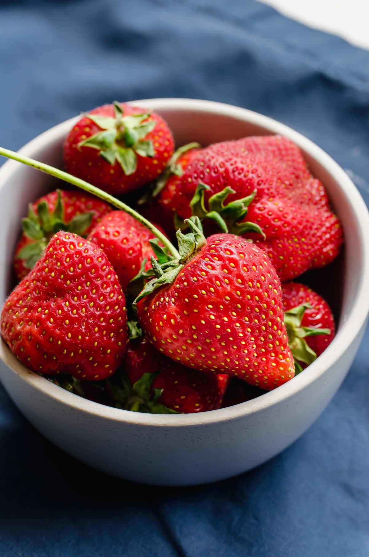 A bowl of fresh strawberries on a blue dish towel. 