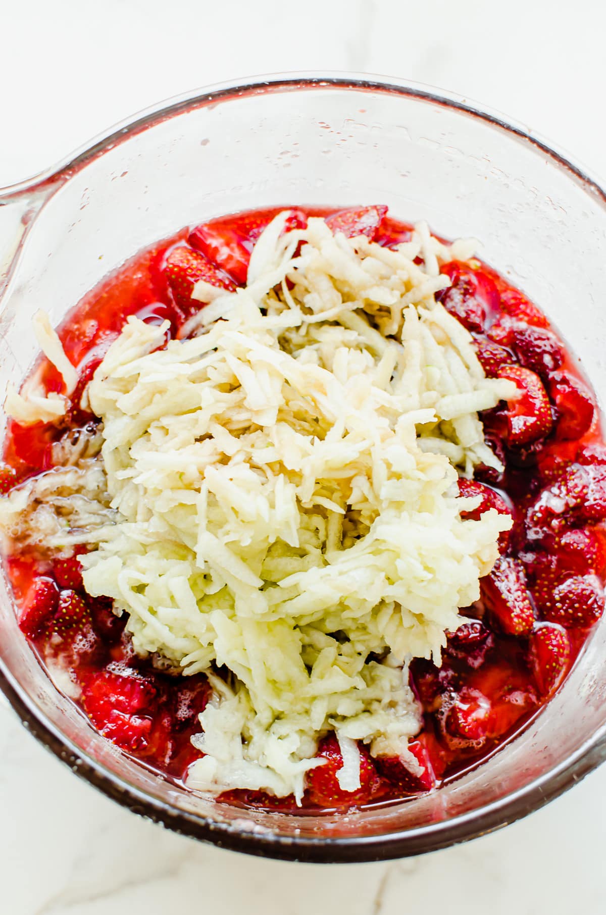 Grated apple being mixed into a bowl of marinated strawberries.